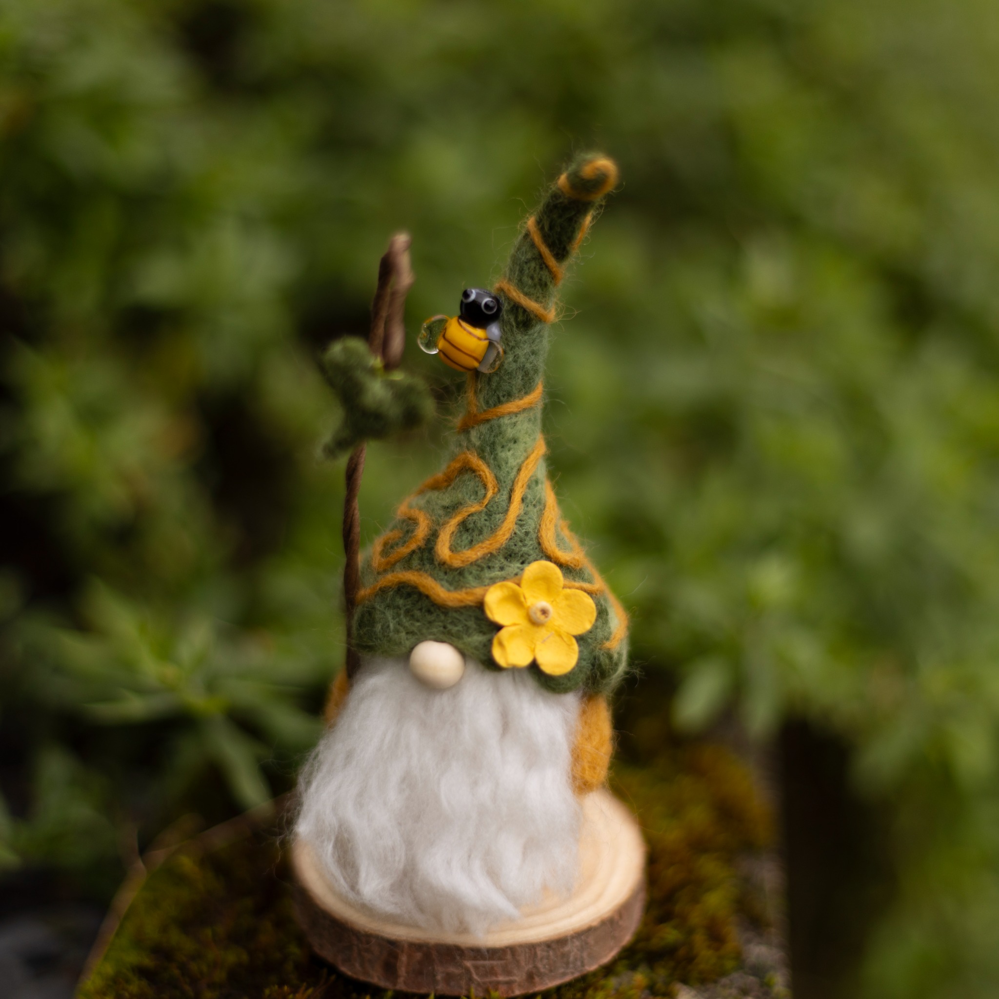 Needle-felted gnome with green hat, bee detail, and yellow flower.